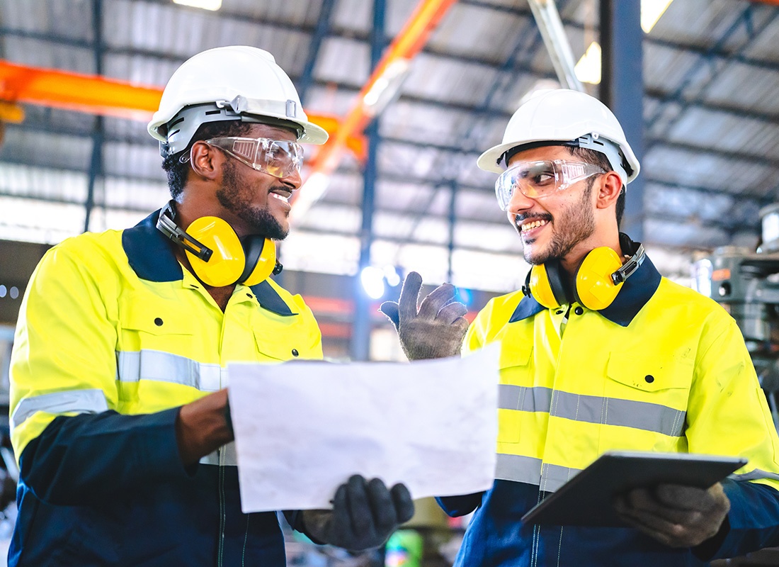 Insurance by Industry - Portrait of Two Men Wearing Hard Hats Discussing Work Procedures While Standing Inside a Manufacturing Facility